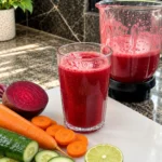 Fresh Beetroot Carrot Cucumber Lime Juice in a tall glass with vegetables and blender