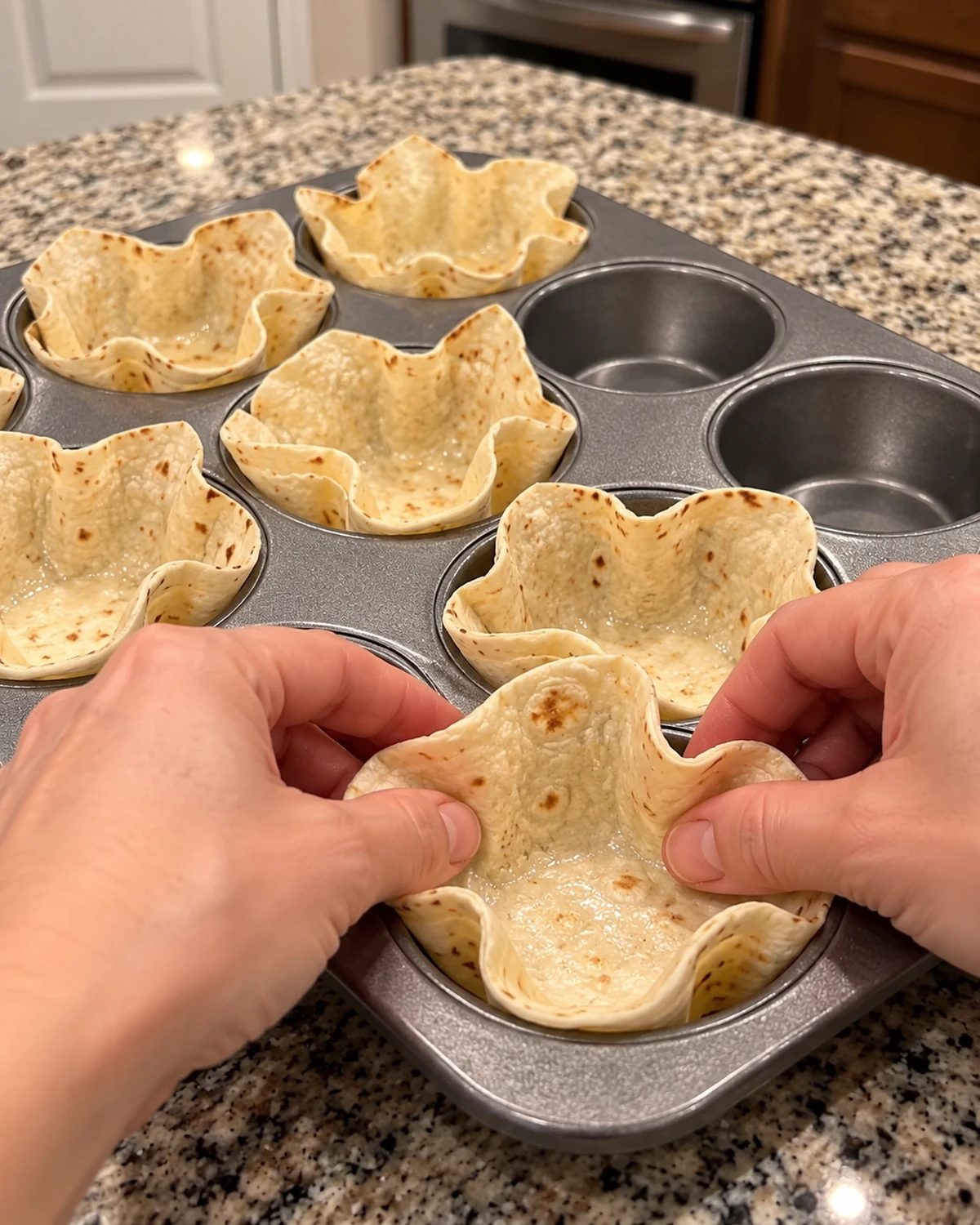Soft flour tortillas being pressed into a 12-cup muffin pan to form edible bowls