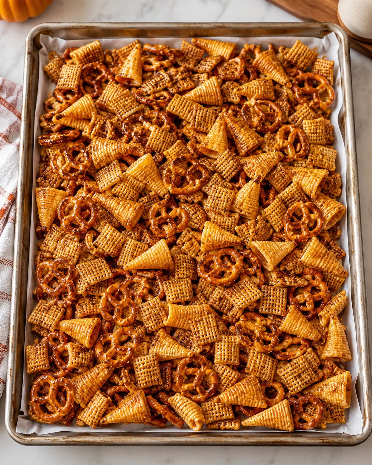 Coated Halloween Chex Mix spread on a parchment-lined baking sheet before baking