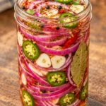 Jar of spicy garlic pickled red onion rings and green jalapeño slices in seasoned brine